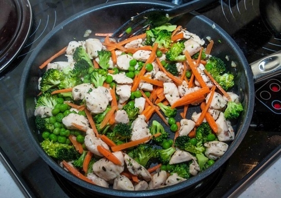 В сковороду с курицей добавим морковь, консервированный горошек и брокколи